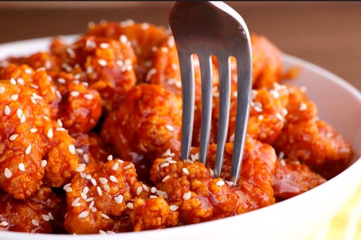 Korean Fried Chicken in bowl with sesame seeds and fork