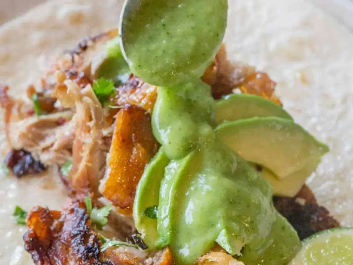 avocado sauce on top of chicken on a tortilla 