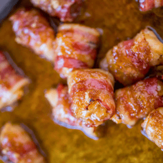 caramelized pork strip wrapped around a piece of poultry stacked on one another on a baking sheet