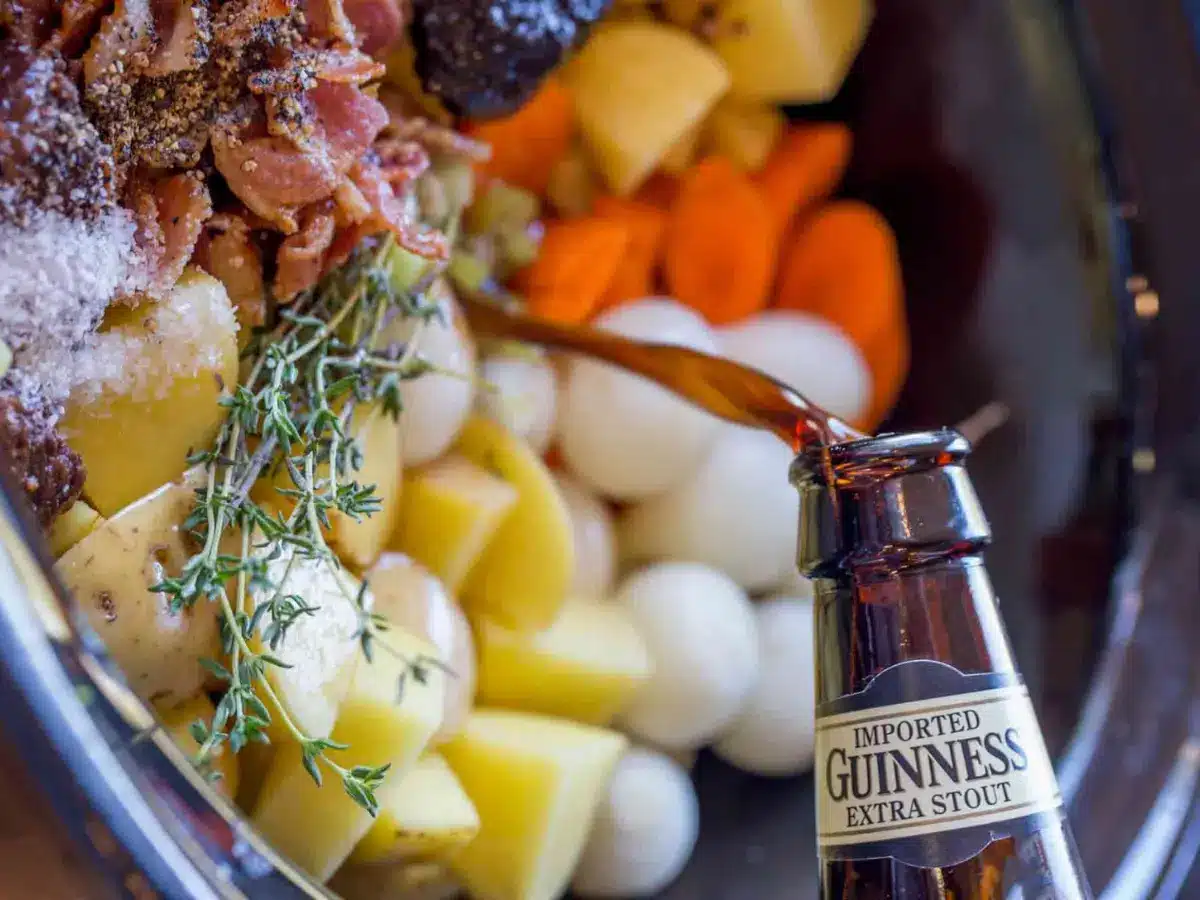 Guinness beer being poured in crockpot with uncooked stew