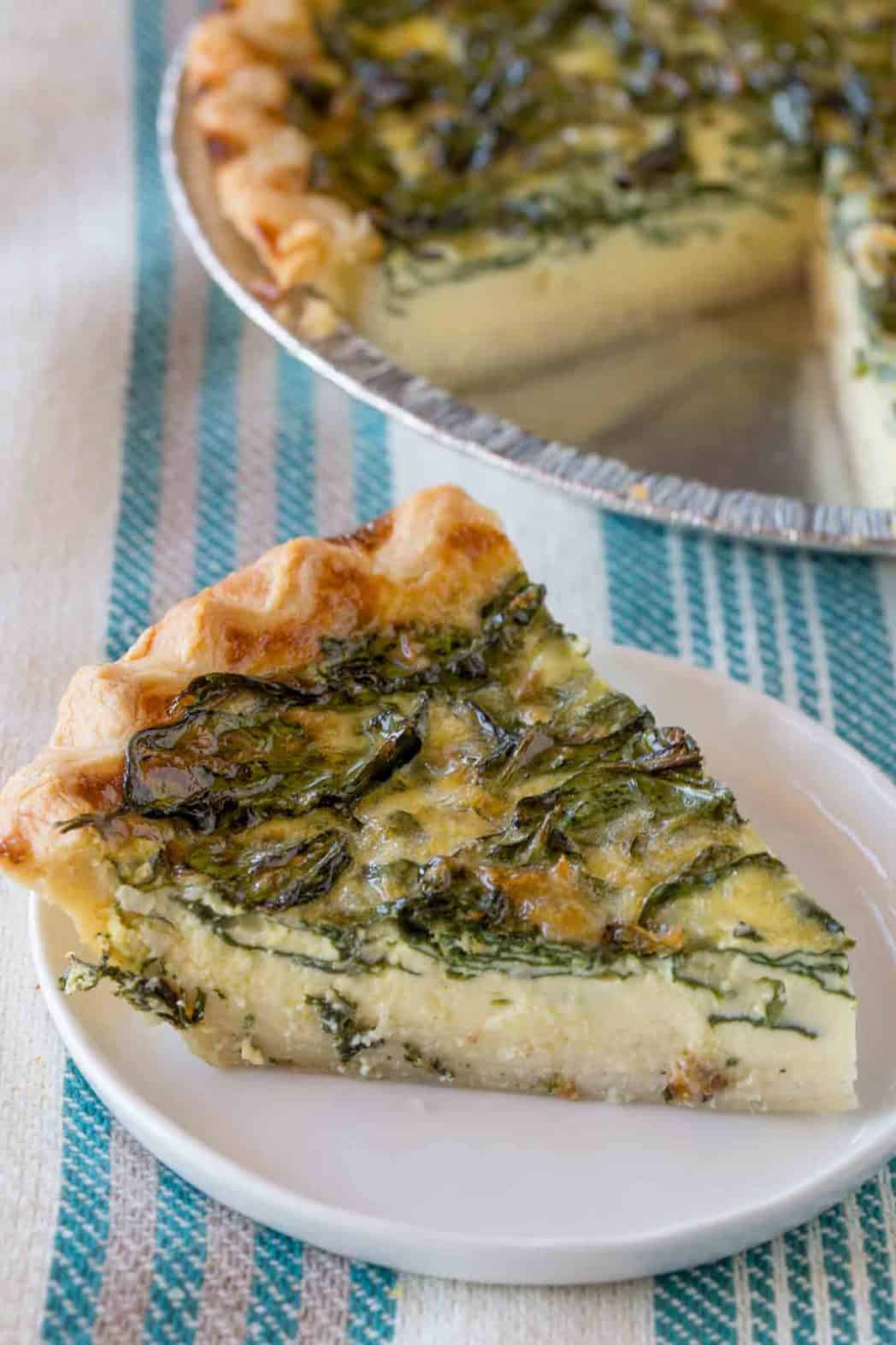 Slice of quiche on a white plate with pie plate in the background
