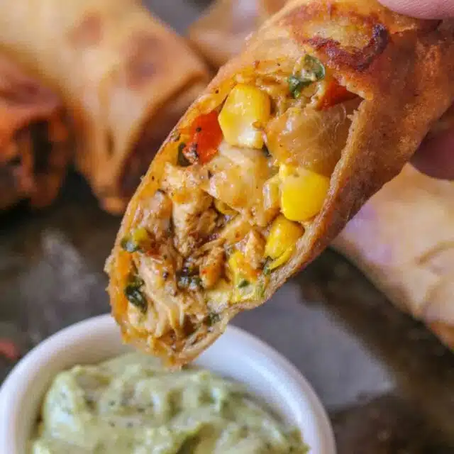 Cheesecake Factory Tex Mex Egg Rolls holding half egg roll over dipping sauce