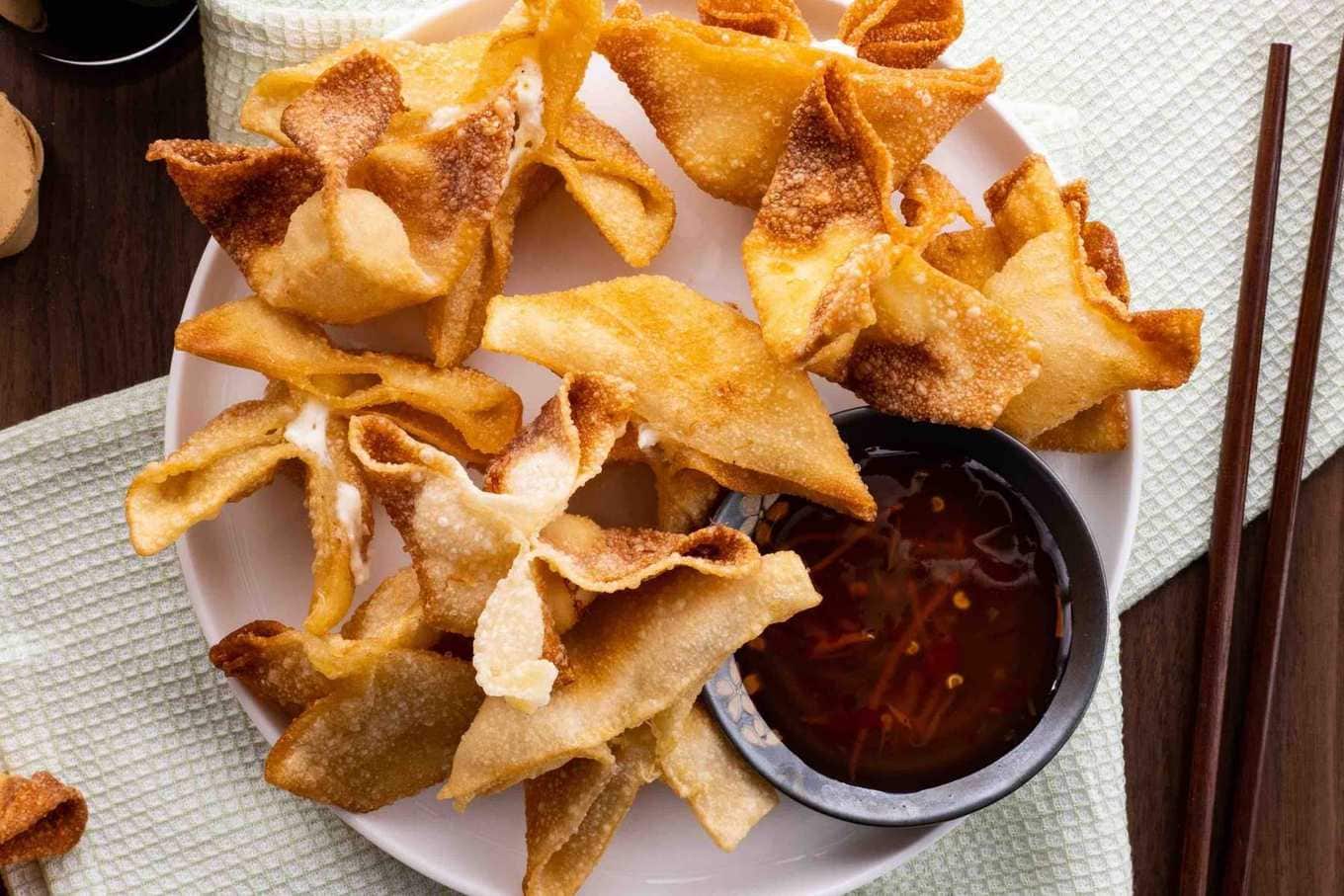 Crab Rangoon on serving plate with dipping sauce and chopsticks