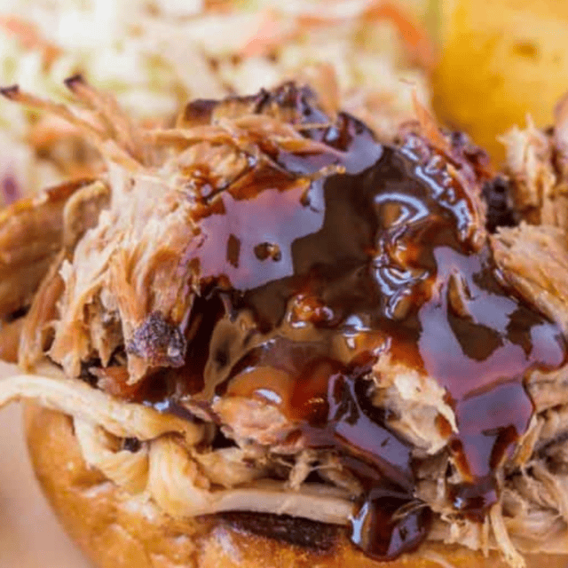 pork on a bun with bbq sauce. coleslaw in background