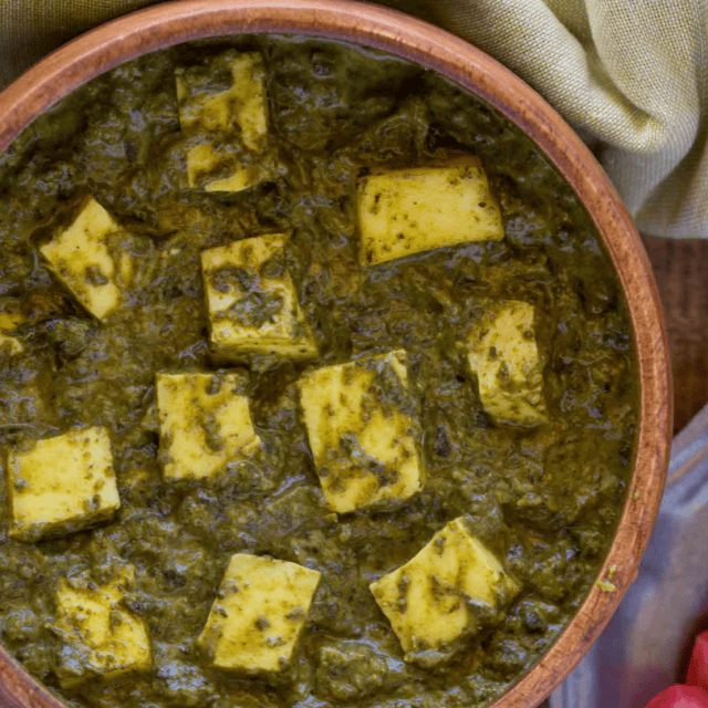 Bowl of Saag Curry with pieces of Paneer in a brown bowl.