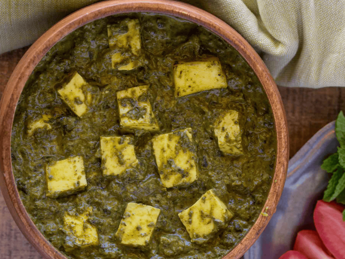 Bowl of Saag Curry with pieces of Paneer in a brown bowl. 