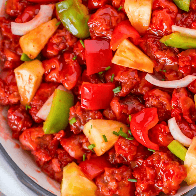 red colored pork in skillet with veggies and pineapples