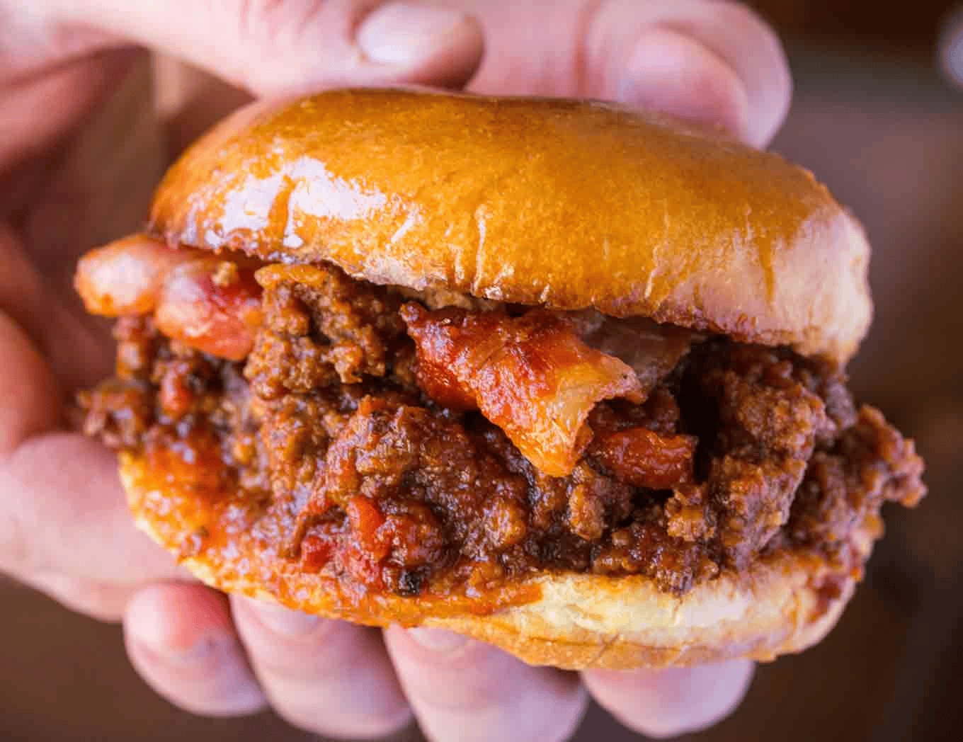 Hand holding a bacon and ground beef sandwich