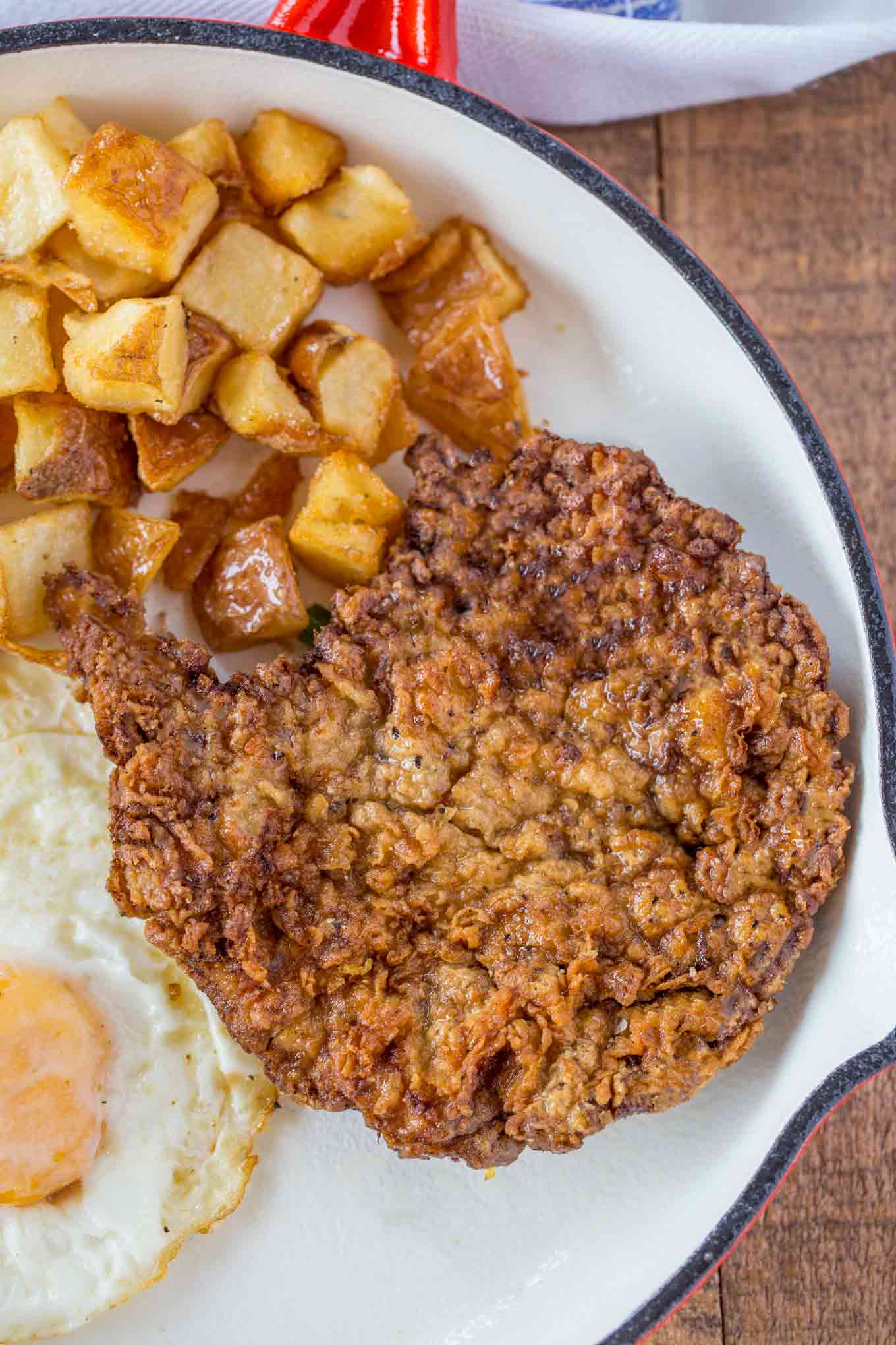 a-white-plate-topped-with-fried-chicken-covered-in-gravy-next-to-green-peas