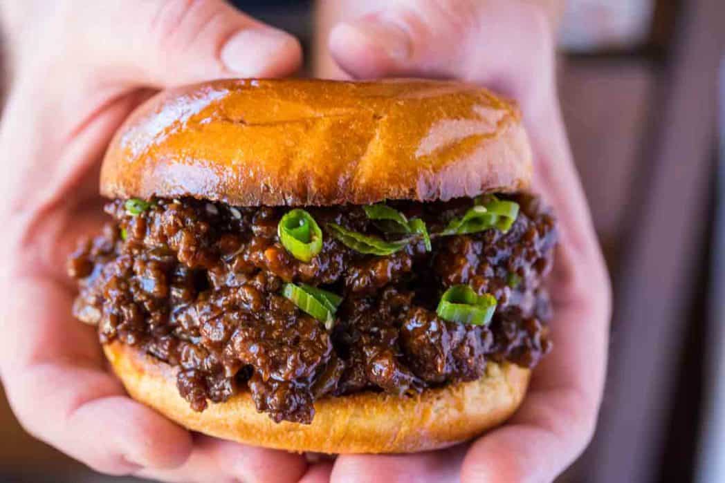 hands holding ground beef sandwich