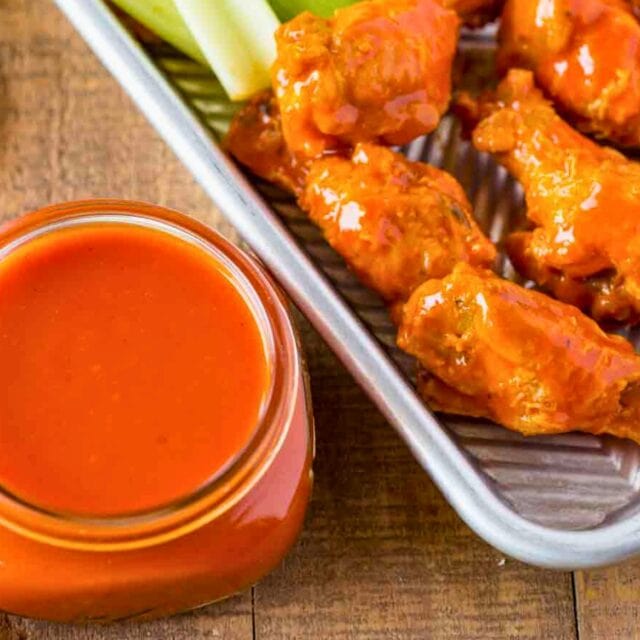 Buffalo Sauce in a jar next to chicken wings