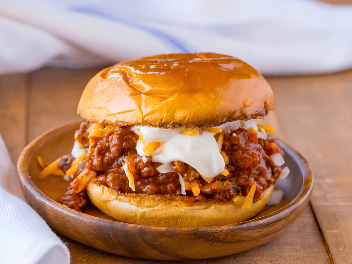 saucy beef, beans, cheese, and sour cream in between two burger buns on a plate
