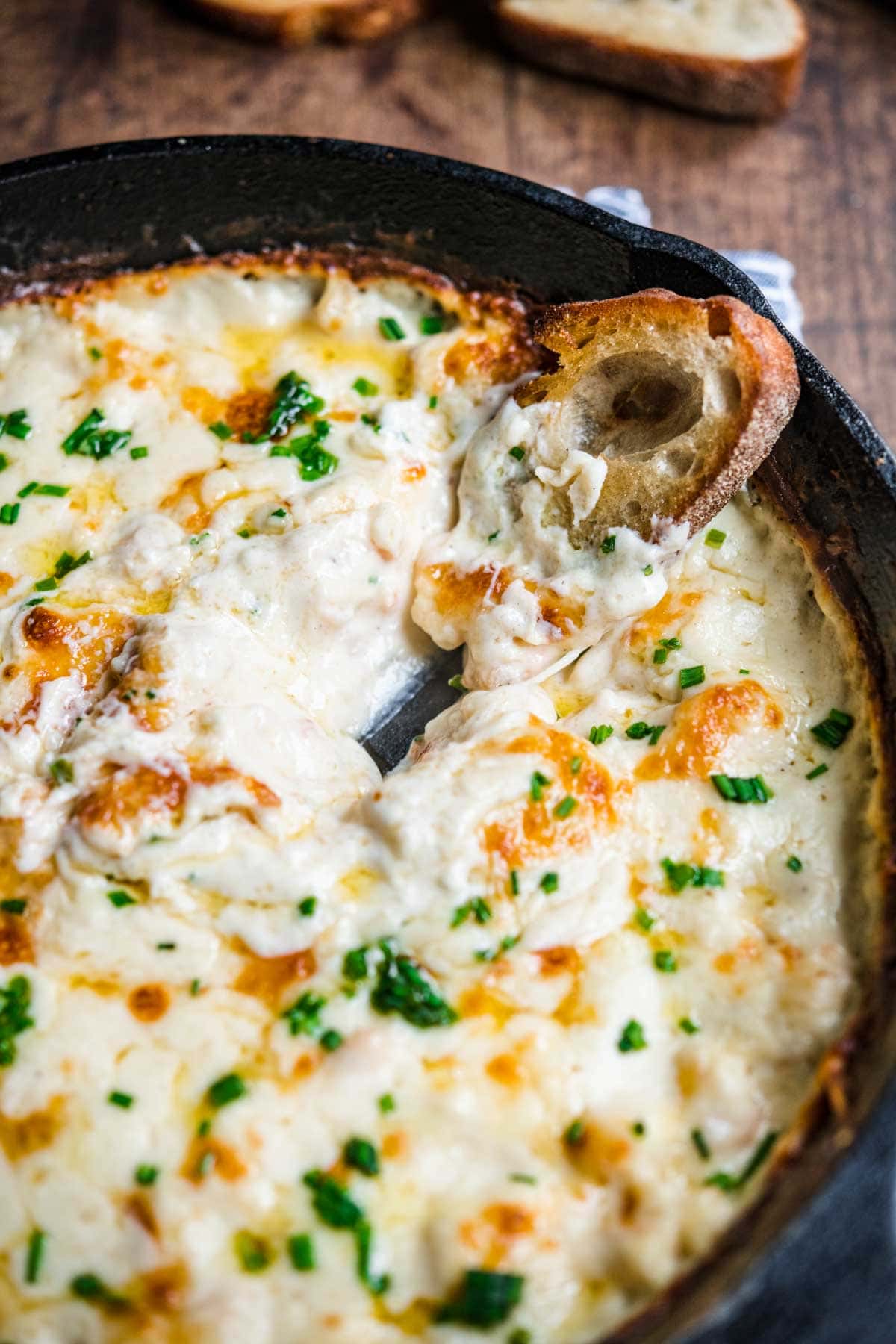 Garlic Shrimp Dip shrimp in skillet after baking with melted cheese and parsley garnish, hand dipping bread