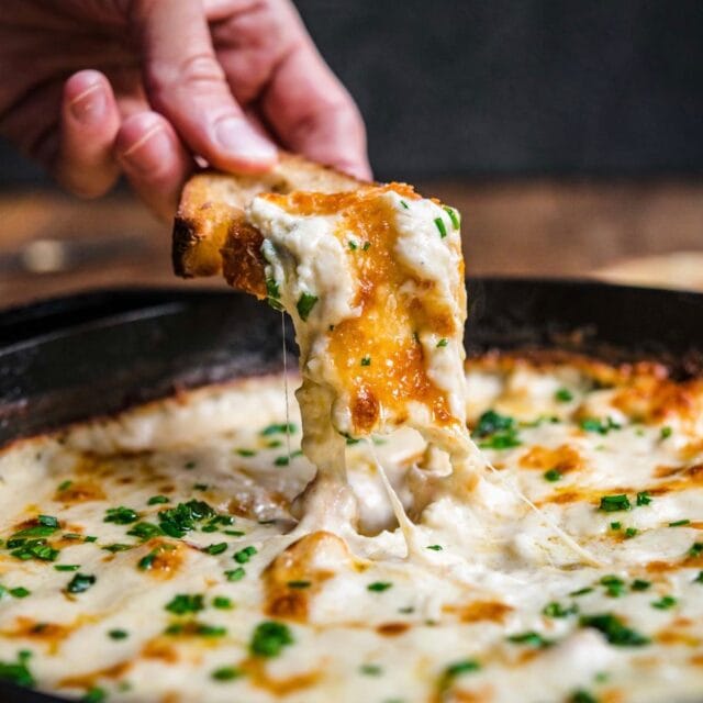 Garlic Shrimp Dip shrimp in skillet after baking with melted cheese and parsley garnish, hand dipping bread