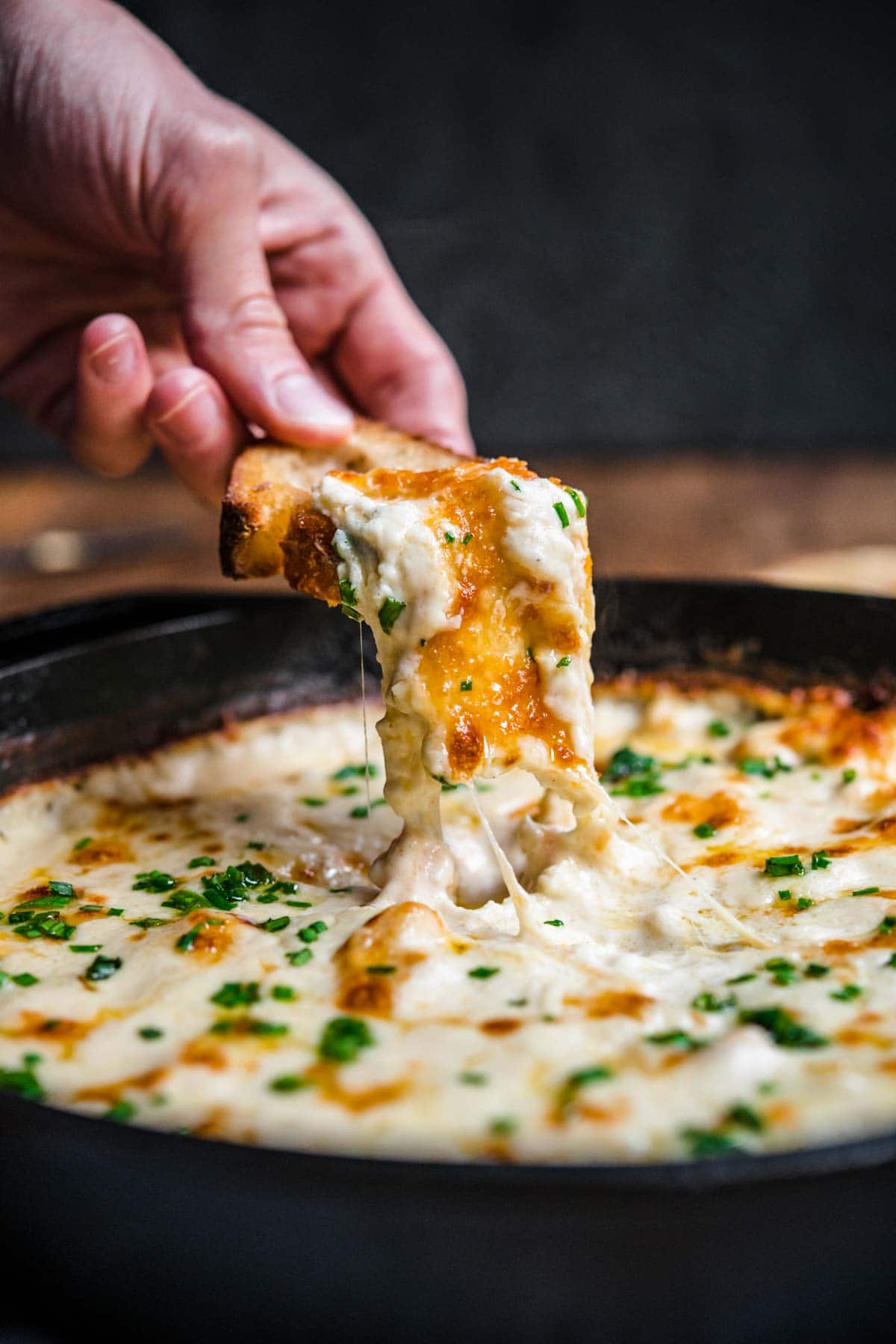 Garlic Shrimp Dip shrimp in skillet after baking with melted cheese and parsley garnish, hand dipping bread