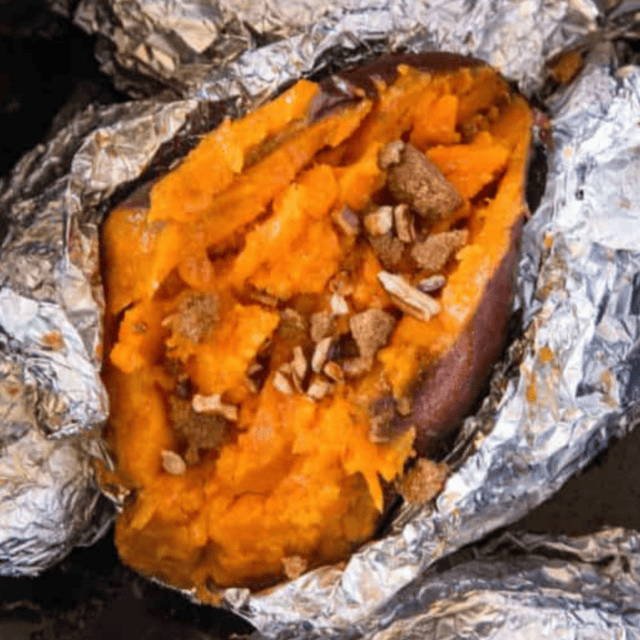 Baked sweet potato topped with butter and brown sugar in foil packet.