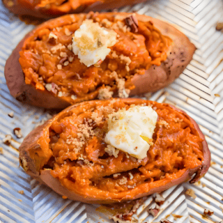 two orange potatoes on a baking sheet with a slice of butter on top