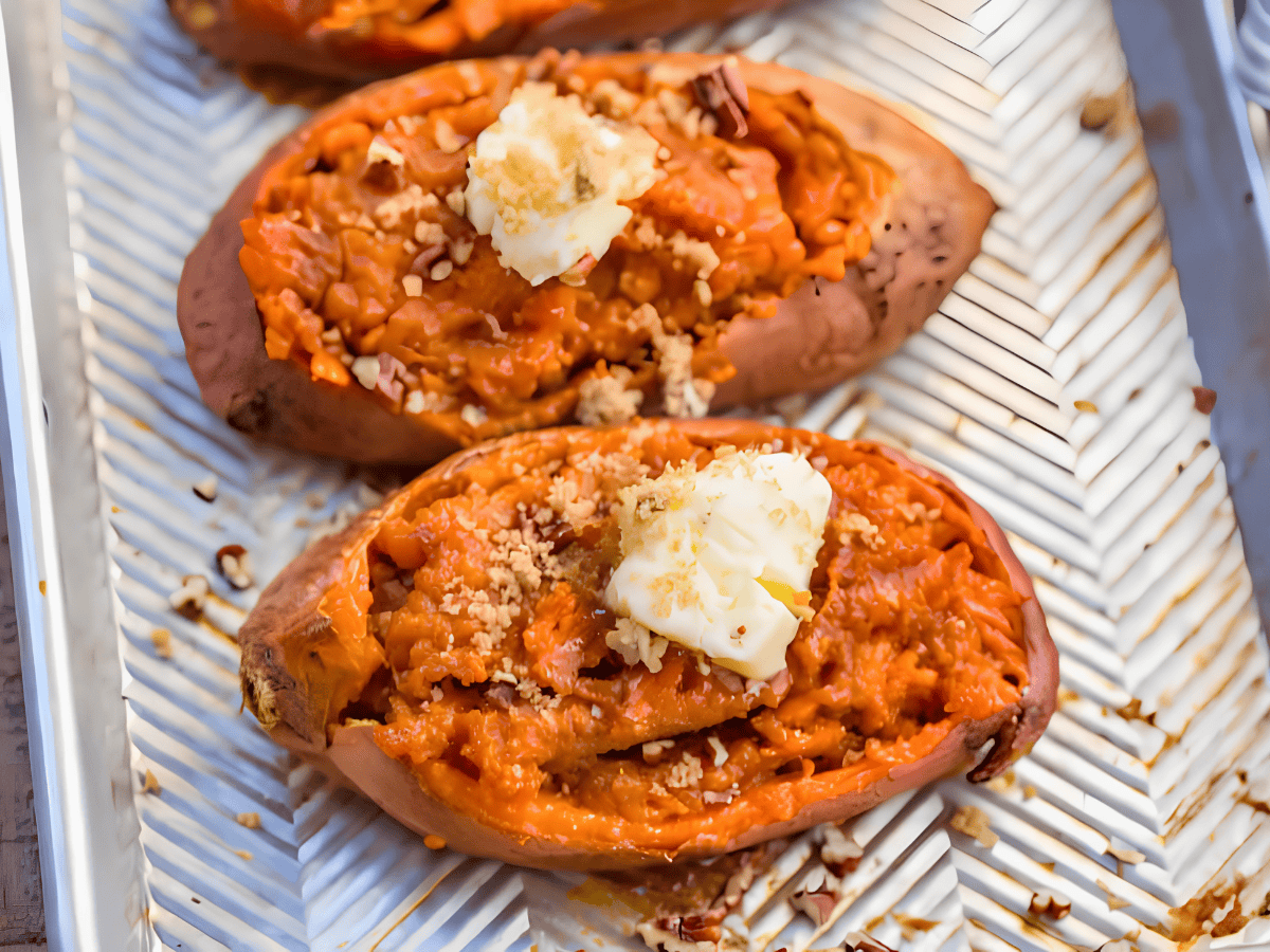 two orange potatoes on a baking sheet with a slice of butter on top