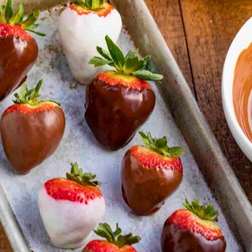 strawberries coated in milk and white chocolate lined up on tray