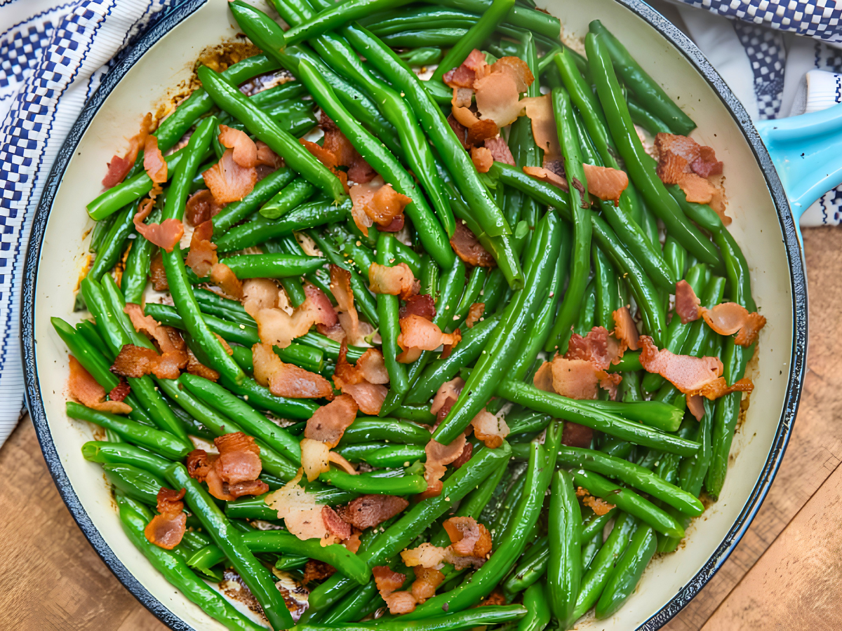 long slender green veggies with cooked bacon in skillet