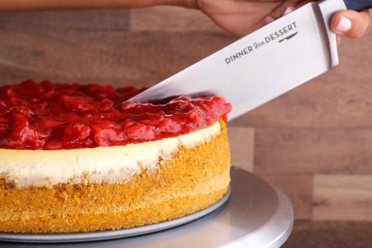 New York Cheesecake on cake plate being sliced with knife