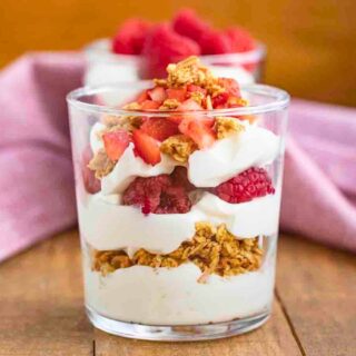Layered yogurt, berries, and granola in small glass cup