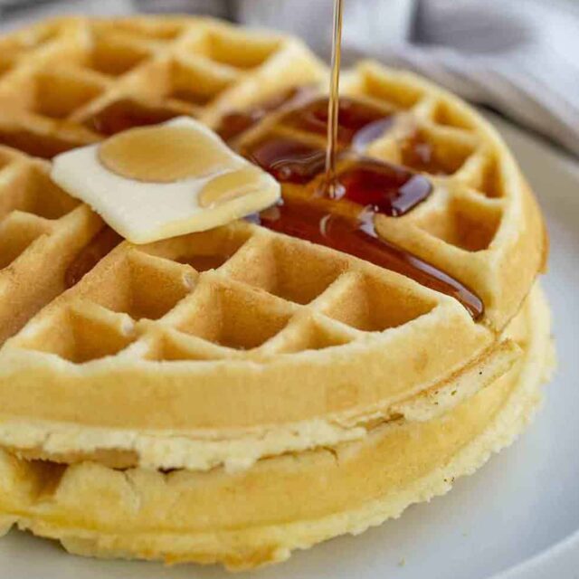 golden, crispy, and fluffy breakfast treat stacked on another on top of a plate with syrup and butter