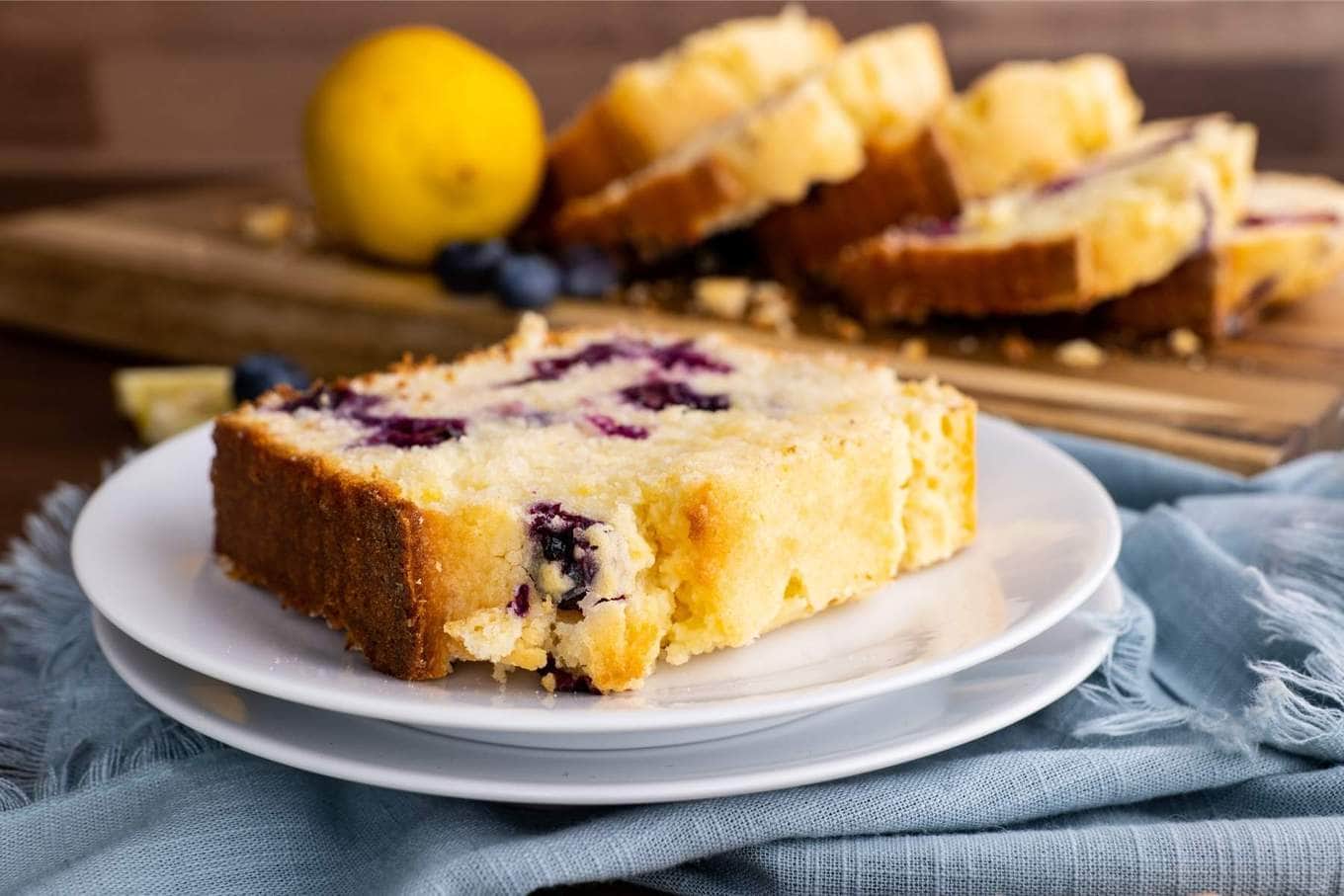 Blueberry Lemon Bread slice on plate with lemon wedges and blueberries