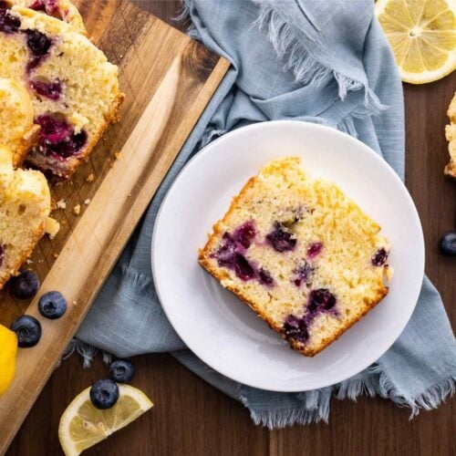 Blueberry Lemon Bread slice on plate with lemon wedges and blueberries