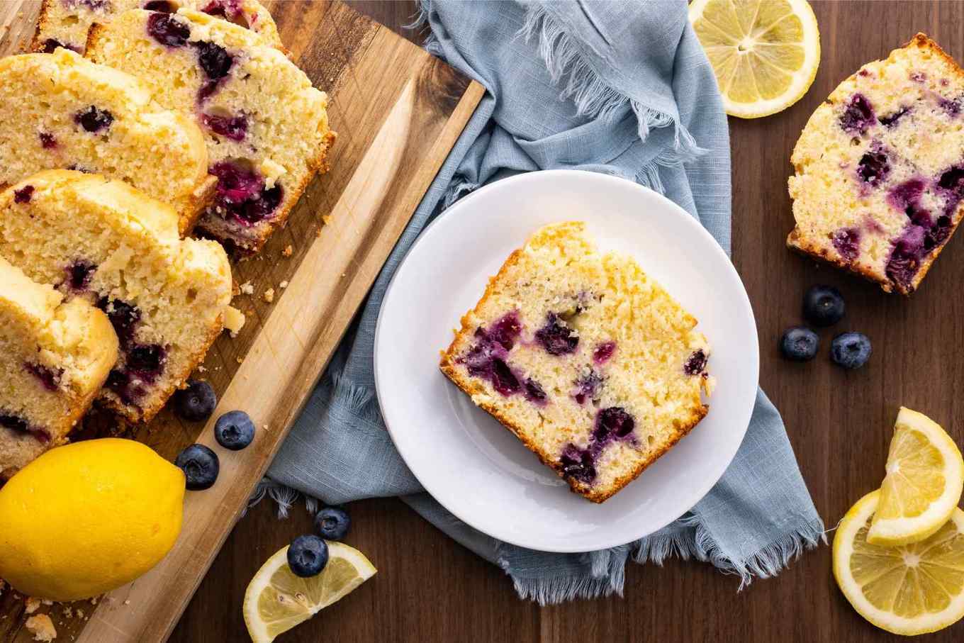 Blueberry Lemon Bread slice on plate with lemon wedges and blueberries