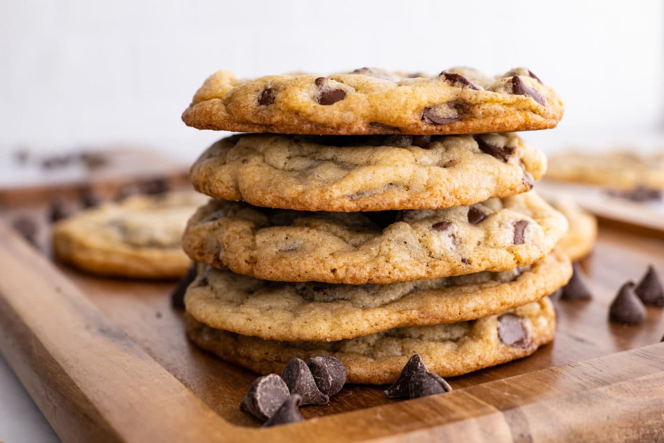 Chocolate Chip Cookies stacked on board with chocolate chips