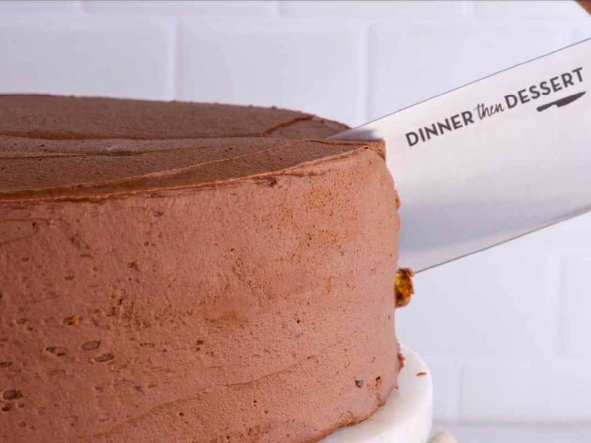 Knife slicing cake with chocolate frosting