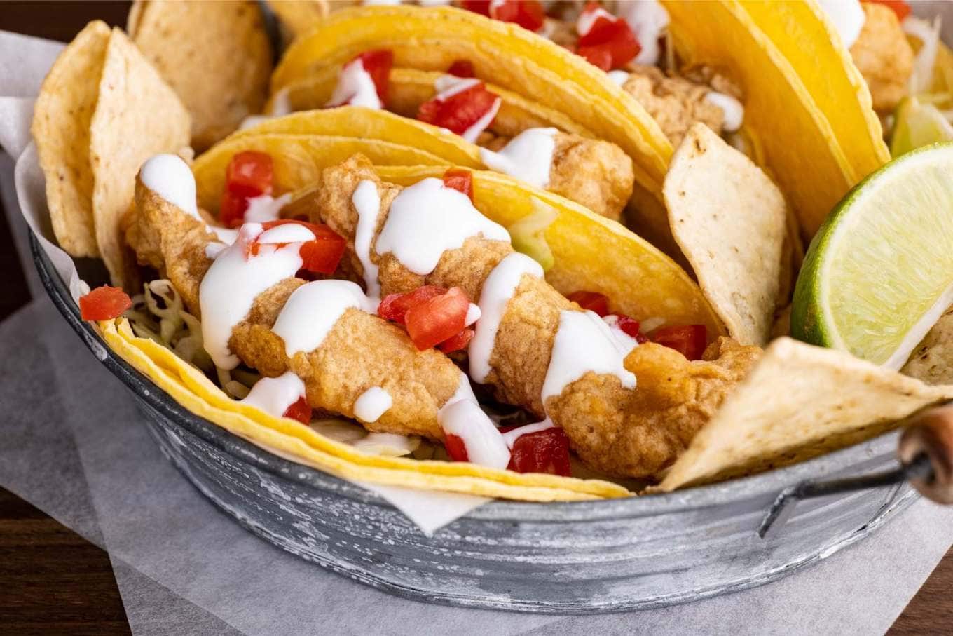 Beer Battered Crispy Fish Tacos in basket with lime wedges