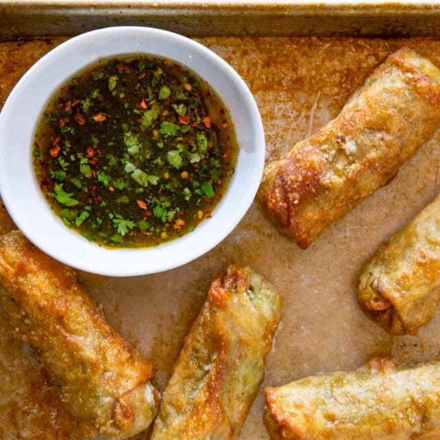 Egg rolls shown with dipping sauce on baking sheet 4x3