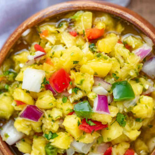 Chopped up fruit, onions, tomatoes, peppers and herbs mixed together in a wood bowl