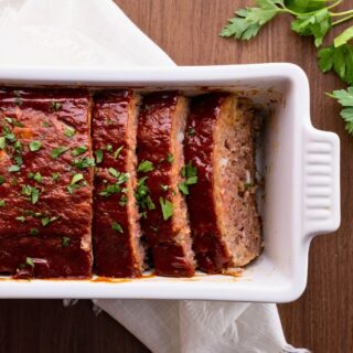Baked meatloaf half whole and half slice in a white loaf baking dish.