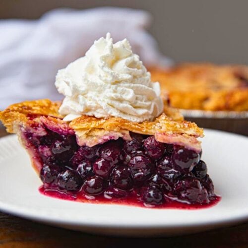 Slice of baked pie on plate with whipped cream.