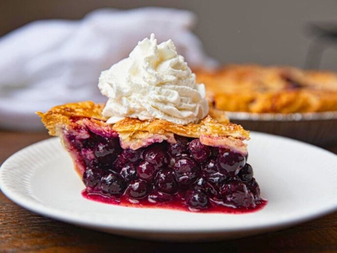 Slice of baked pie on plate with whipped cream.