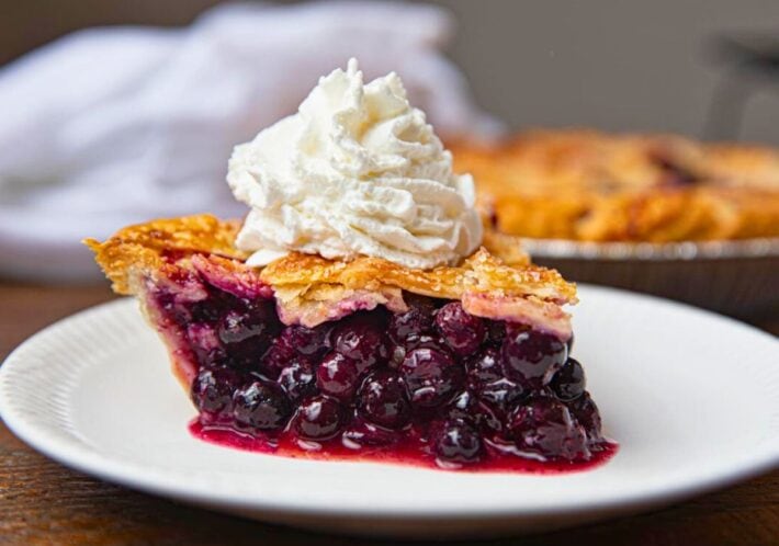 Slice of baked pie on plate with whipped cream.