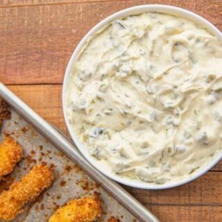 Sauce in a white bowl with a sheet pan of fish sticks next to it.
