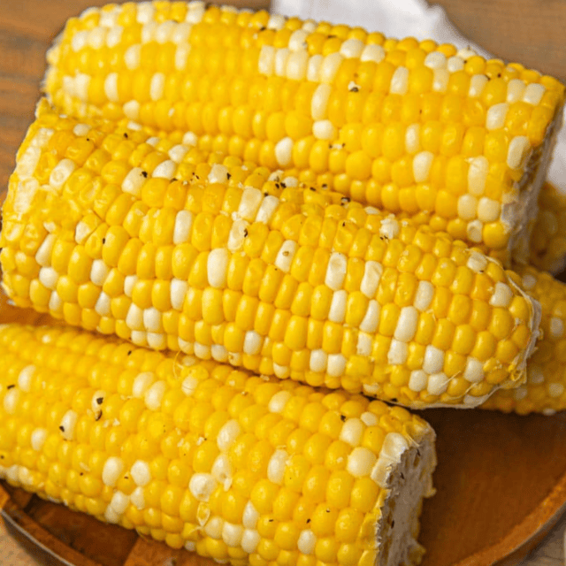 Fresh boiled corn on the cob with yellow and white kernels on a wooden plate.