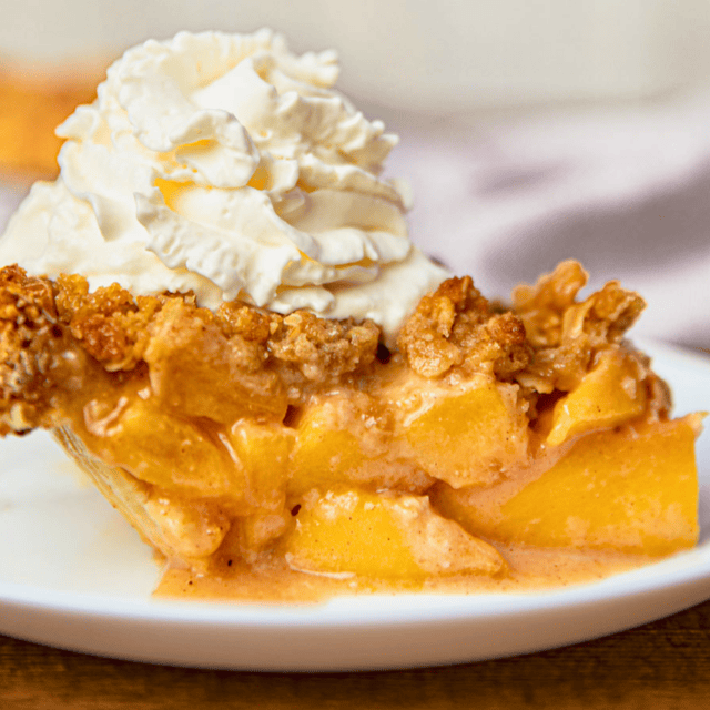 Slice of peach pie on plate topped with whipped cream