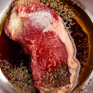 Steak marinating in metal bowl