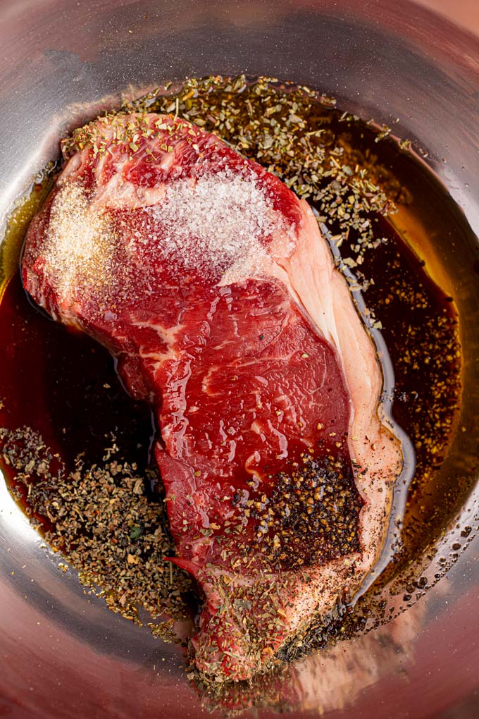 Steak marinating in metal bowl