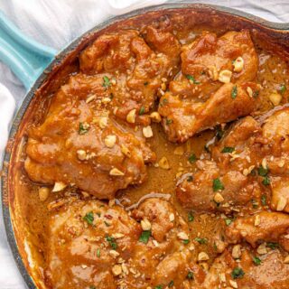 Poultry dish cooking in a frying pan with a blue handle