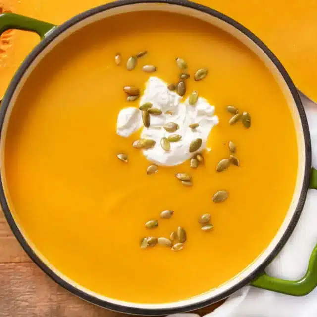 squash soup in a pot topped with soup cream and pumpkin seeds