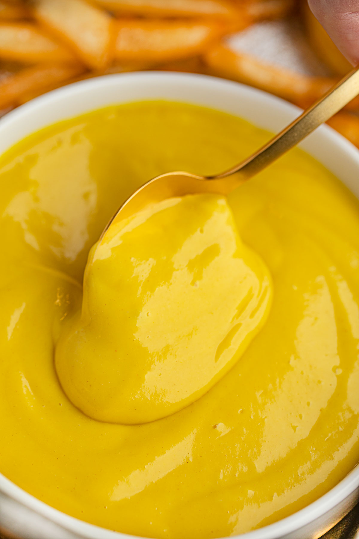 Bowl of honey Mustard with spoon and fries in the background.