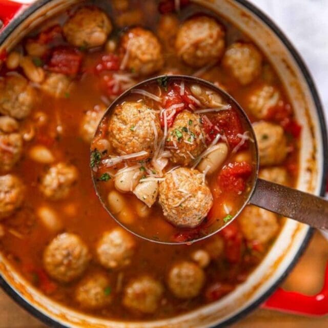 A white pot of soup with a ladle full of soup ready to serve.