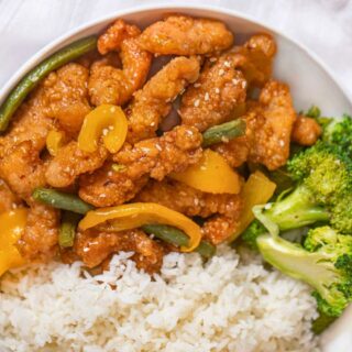 Prepared honey sesame chicken pieces in bowl with broccoli and rice.