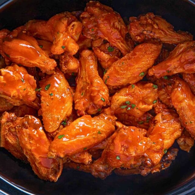 Cooked buffalo wings in slow cooker insert.